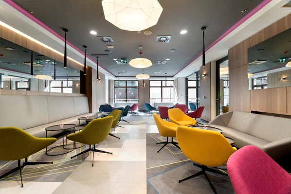 A modern waiting area with colorful chairs, a sofa, and a large geometric light fixture. - Golden Tulip Krakow Kazimierz (Kraków)