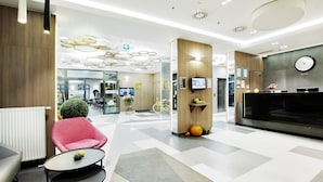 A modern hotel lobby with a reception desk, seating area, and a large TV screen.