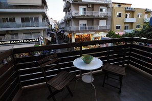 A balcony with wooden chairs and a small table, overlooking a street with shops and buildings. - Marnin Apartments (Rhodes)