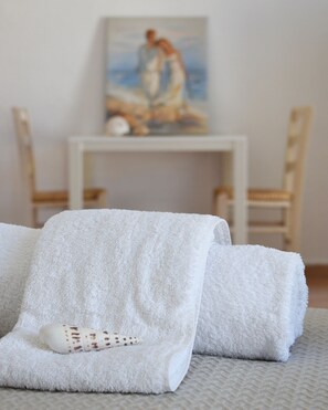 A neatly made bed with two white towels, a decorative bottle, and a painting on the wall. - Marnin Apartments (Rhodes)
