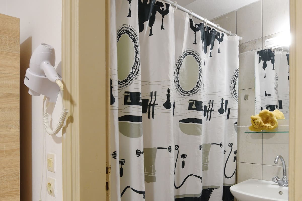 A bathroom with a shower curtain featuring a black and white abstract pattern, a white hairdryer on a wall-mounted stand, a white sink with a faucet, and a mirror above the sink.