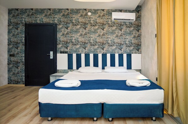 A double bed with a blue and white bedspread, two white pillows, and two towels folded on the bed. There is a black door to the left and an air conditioning unit on the wall above the bed. - Miss Cleopatra Hotel (Alanya)
