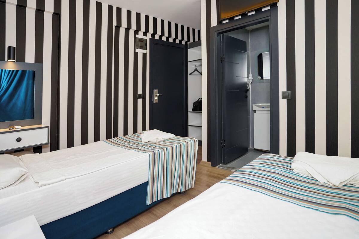 A hotel room with two beds, a TV, a wardrobe, and a bathroom visible through an open door.