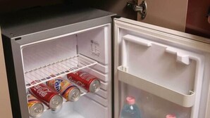 Un réfrigérateur compact doté d’un compartiment congélateur à gauche et d’un compartiment réfrigérateur à droite, contenant des boissons et des conserves.
