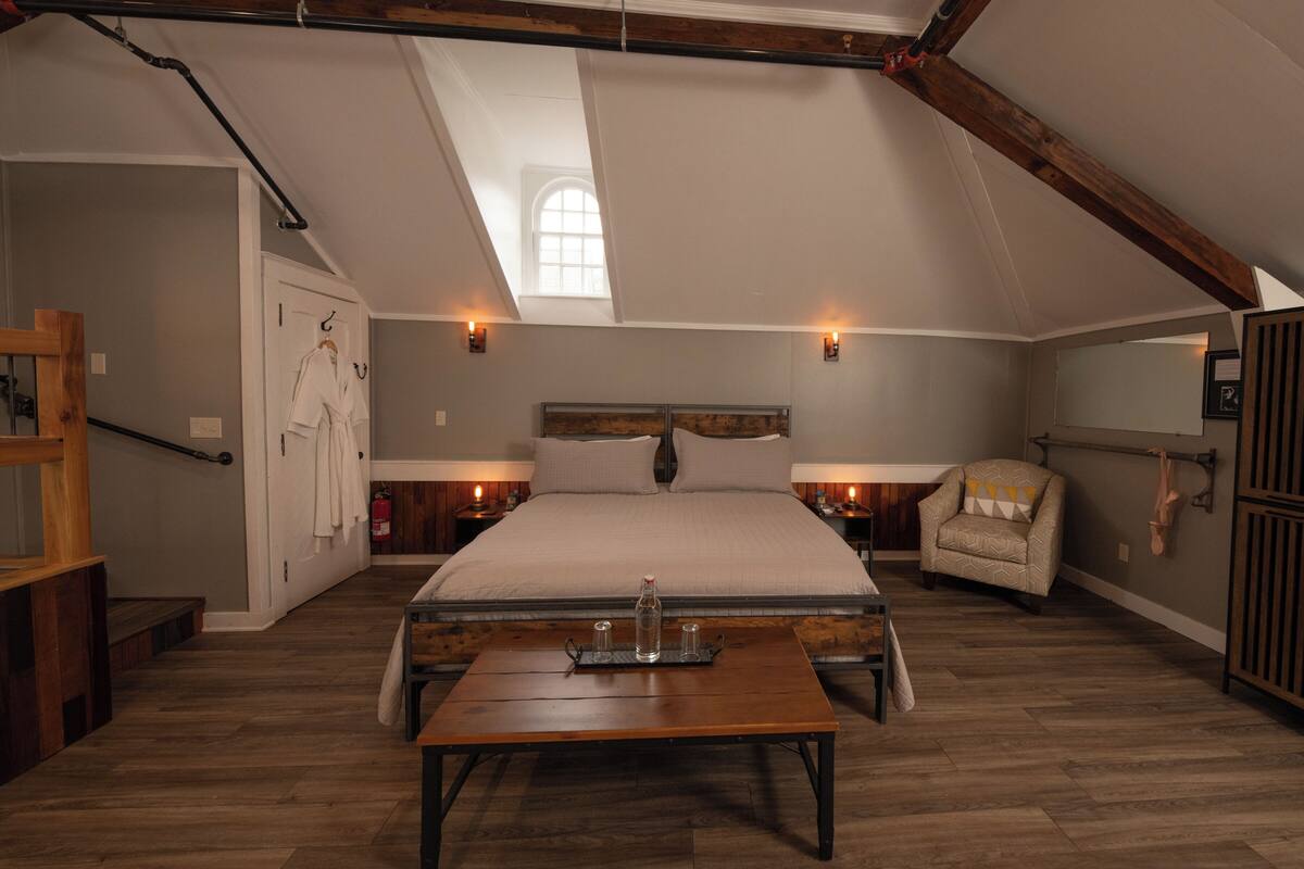 Ein Schlafzimmer mit einem großen Bett, einem Holztisch, einem Stuhl und einem Fenster mit Tageslicht.