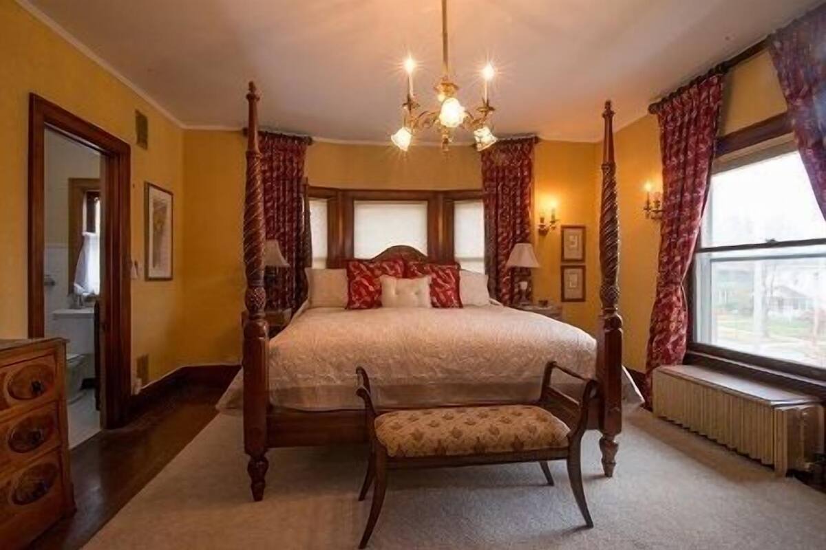 Ein Himmelbett mit Sitzbank, einer Kristallleuchter und Blick ins Freie durch ein Fenster.