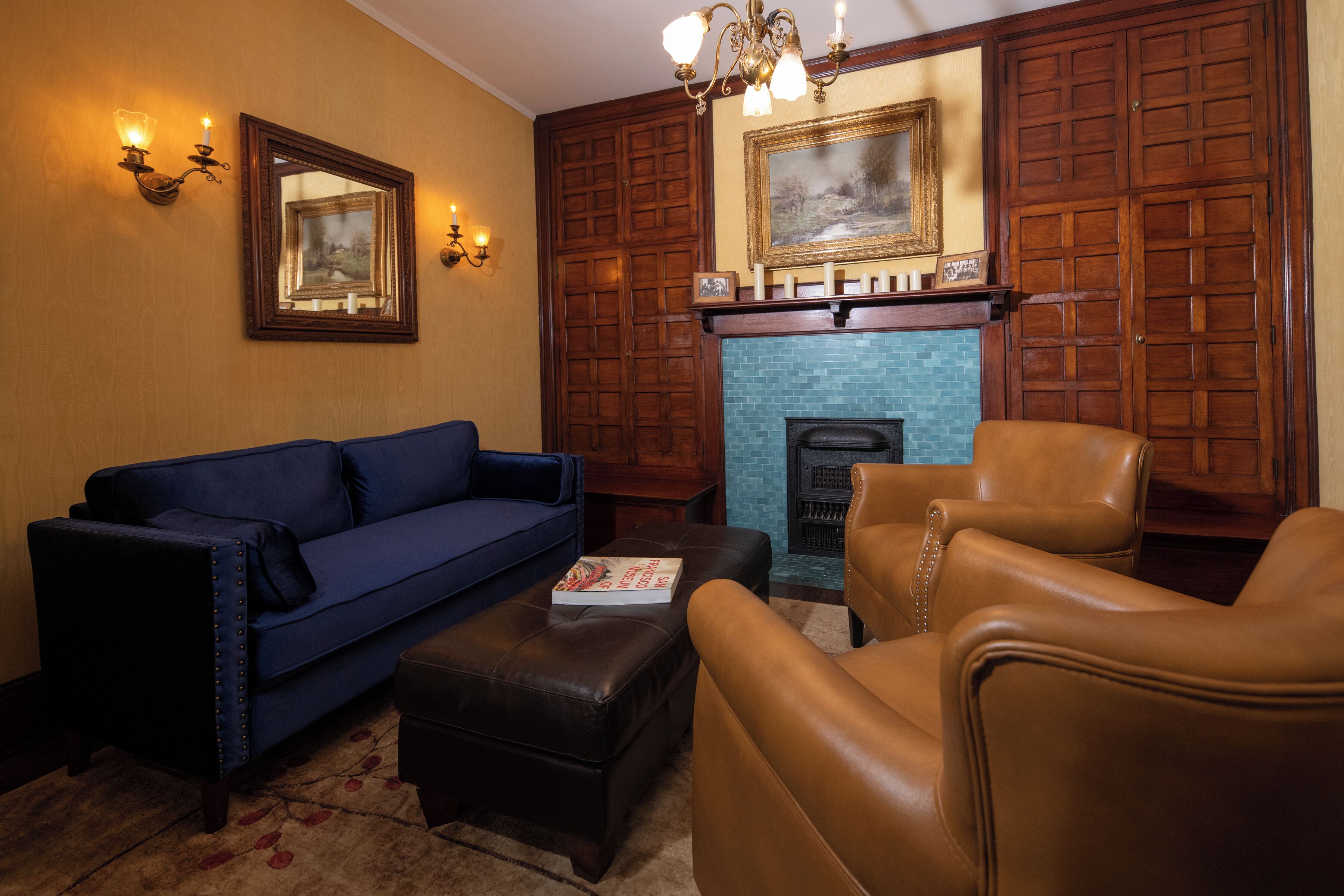 A living room with a blue sofa, a brown leather armchair, a fireplace, and wooden paneling on the walls.