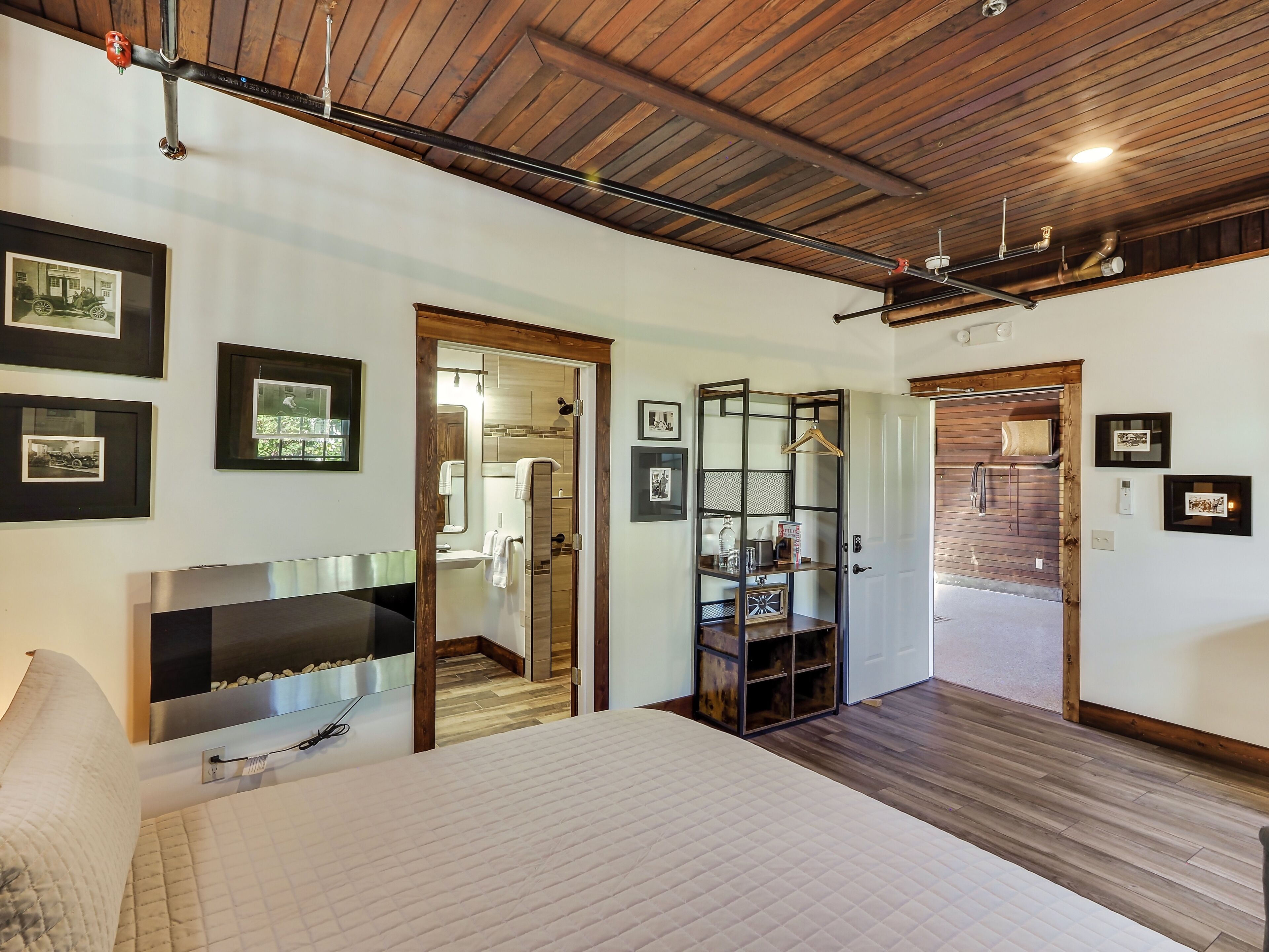 A bedroom with a bed, a TV, and a wooden ceiling. There are framed pictures on the wall and a wooden cabinet.
