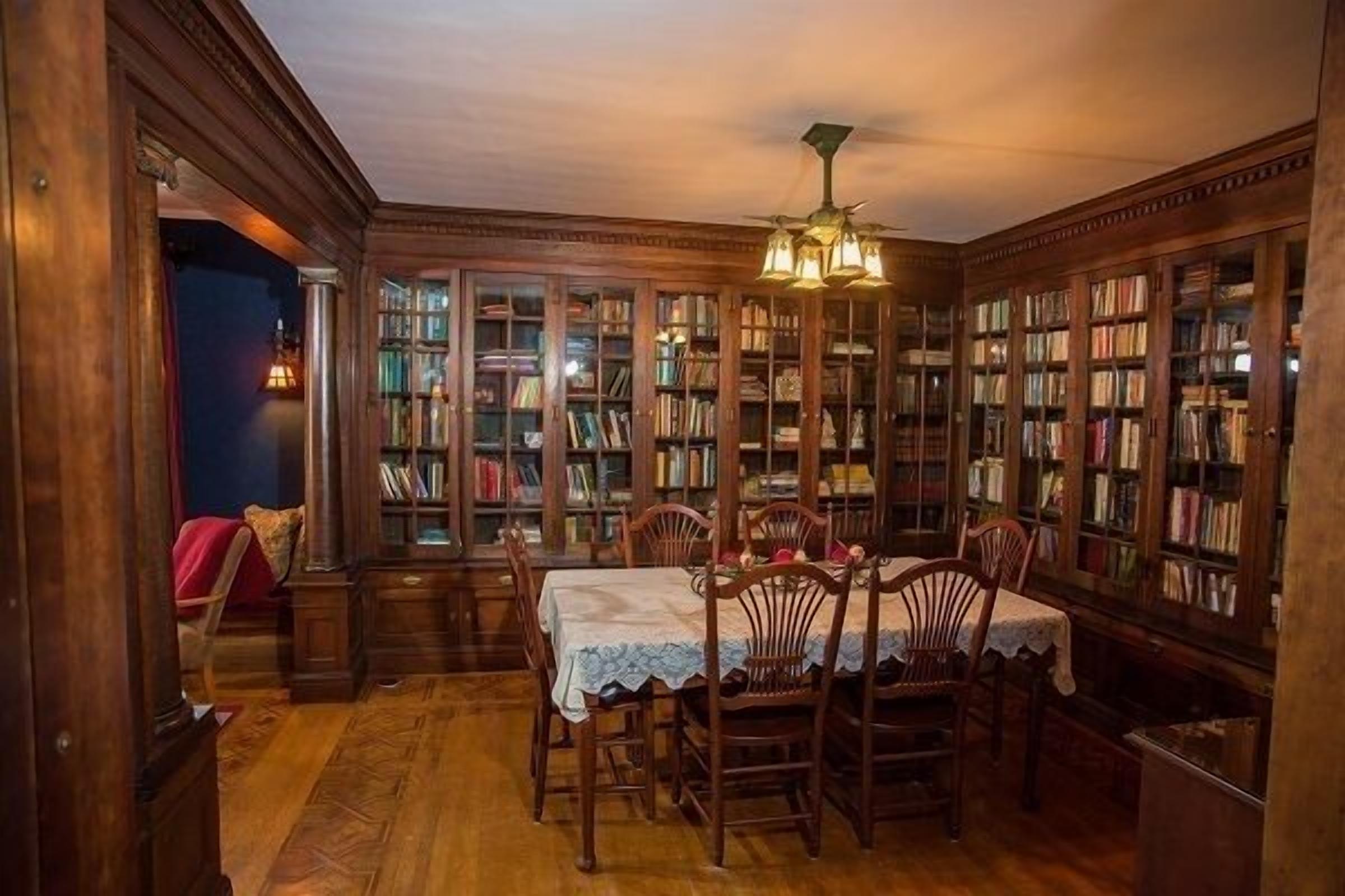 A library with wooden bookshelves, a table with chairs, and a ceiling fan.