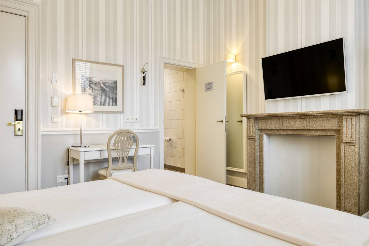 A hotel room with a bed, a desk, a chair, a television, and a fireplace.