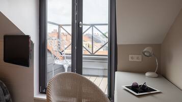 A room with a sliding glass door to a balcony, a wicker chair, a desk with a lamp, and a tablet with glasses on it.