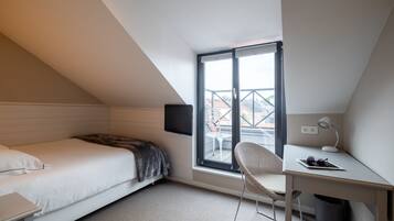 A small, modern bedroom with a bed, a desk, a chair, a TV, and a window with a view of buildings.
