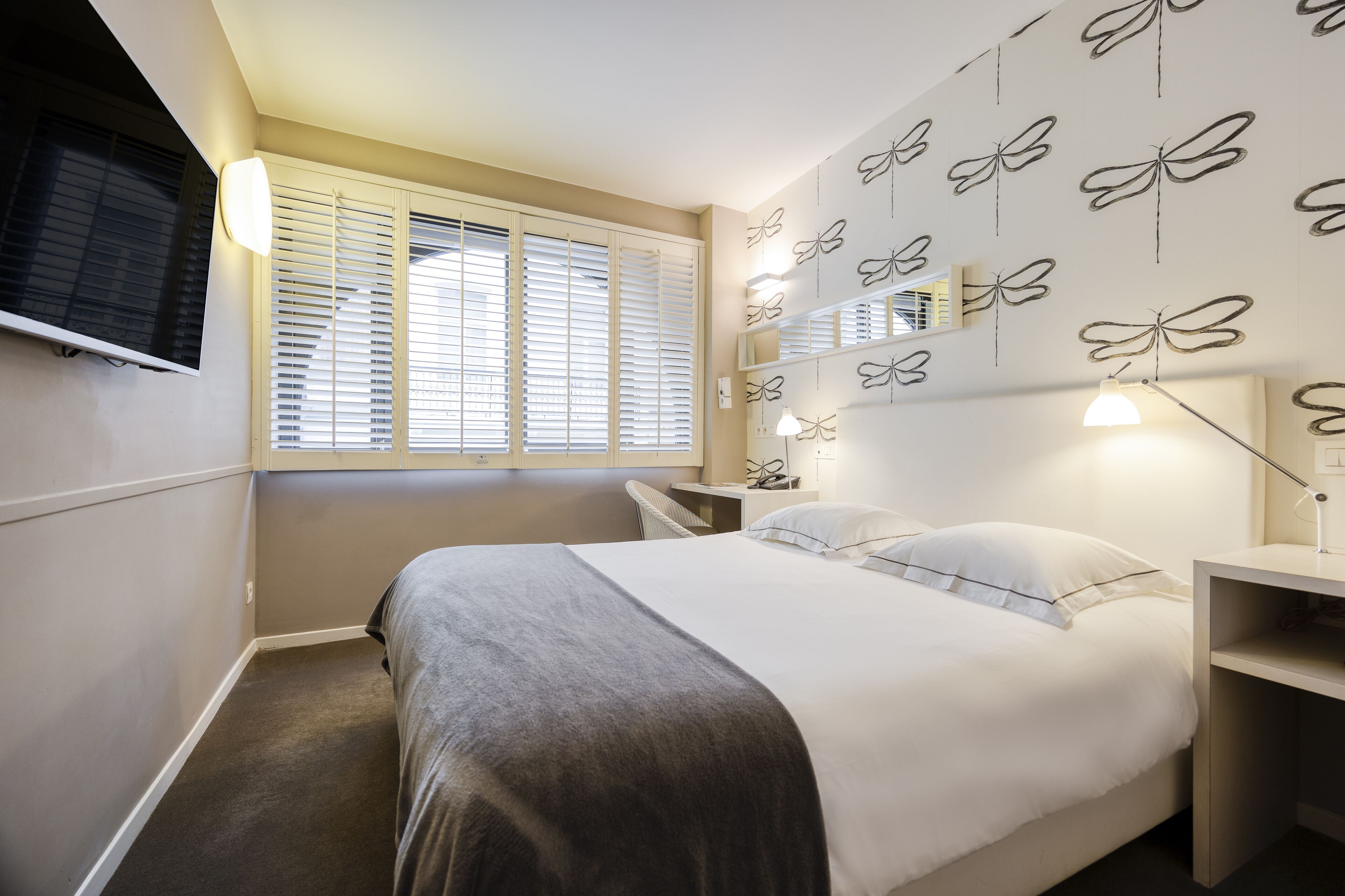 Un dormitorio con cama, mesitas de noche, televisión y ventana con persianas.