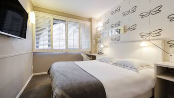 Un dormitorio con cama, mesitas de noche, televisión y ventana con persianas.