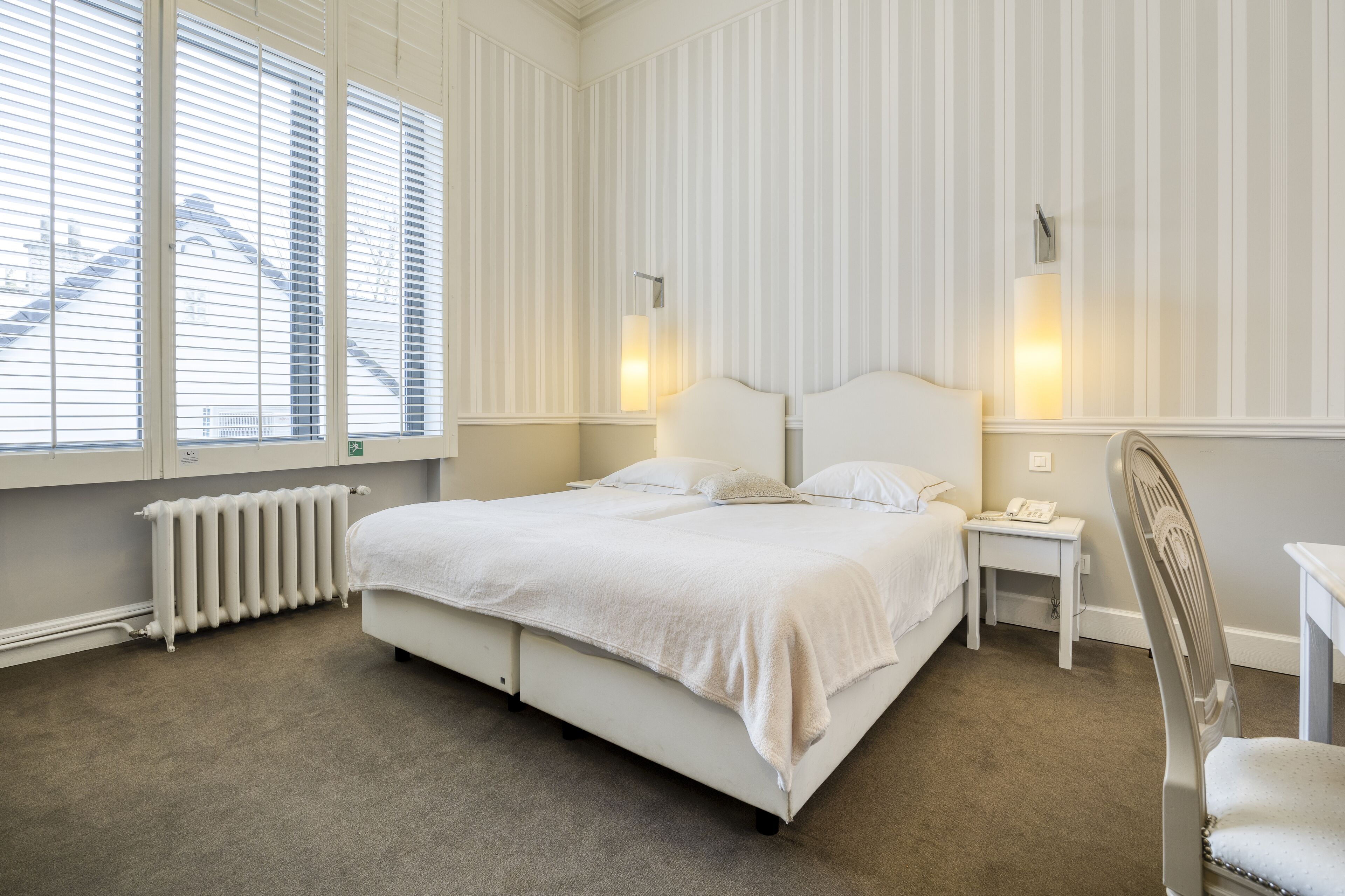 A bedroom with a large bed, a bedside table, a chair, and a radiator.