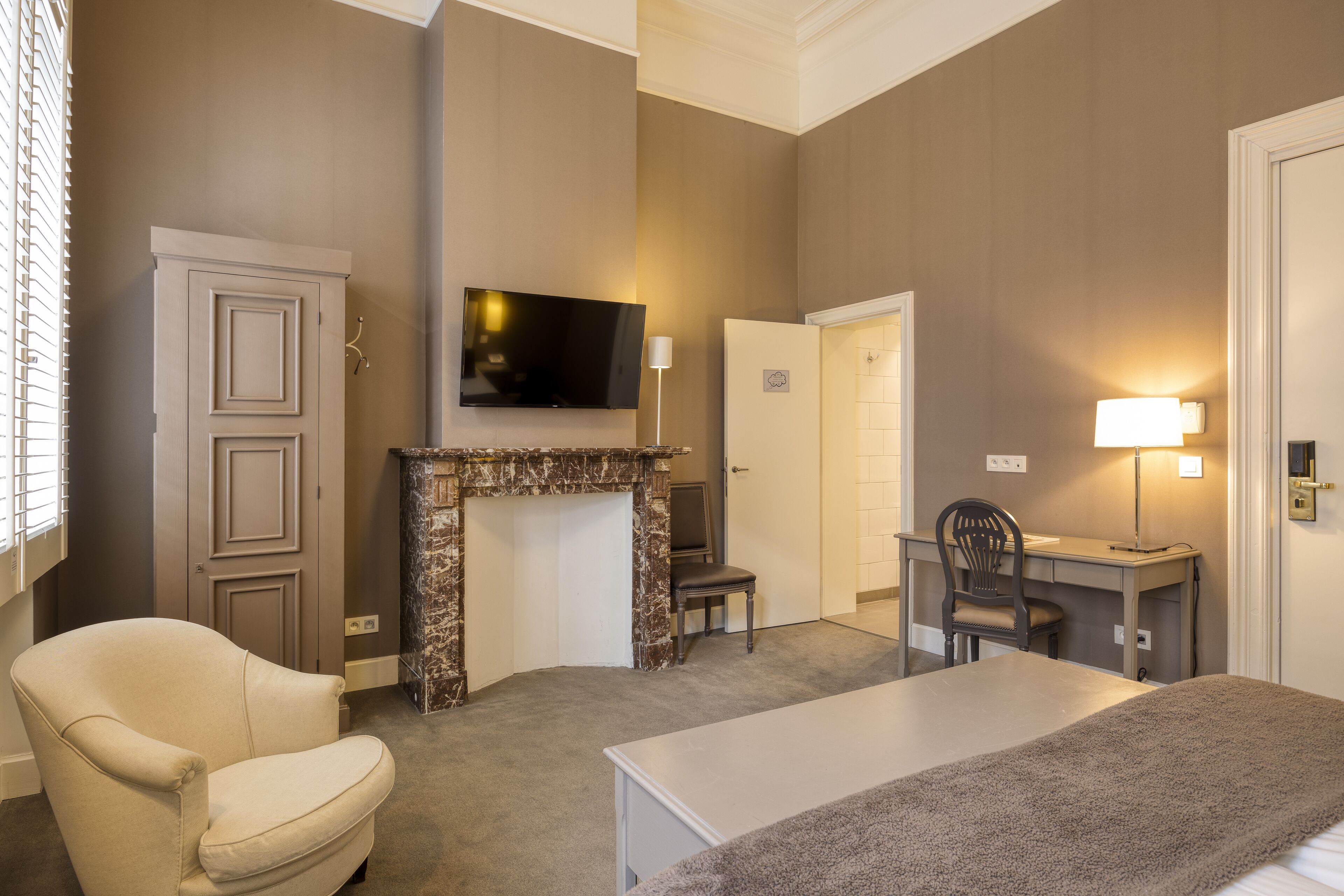 Une chambre d’hôtel avec une cheminée, un téléviseur fixé au mur, un bureau avec une chaise et un lit avec une couverture.