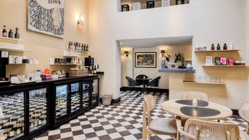 A café with checkered flooring, a bar area with shelves of bottles, wicker chairs, and a table with a candle.