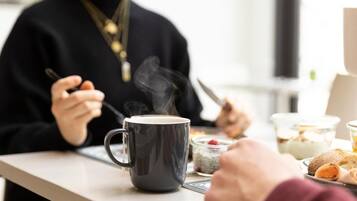 A person sitting at a table with a cup of coffee, a plate of food, and a glass container.