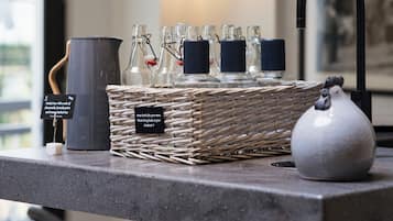 Un espace bar avec un comptoir, une carafe, un panier rempli de verres et un coq en céramique.