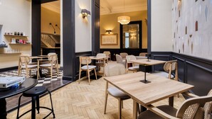 L’intérieur d’un restaurant est agrémenté de tables et de chaises en bois, d’un parquet à motifs en chevrons et de luminaires fixés aux murs.