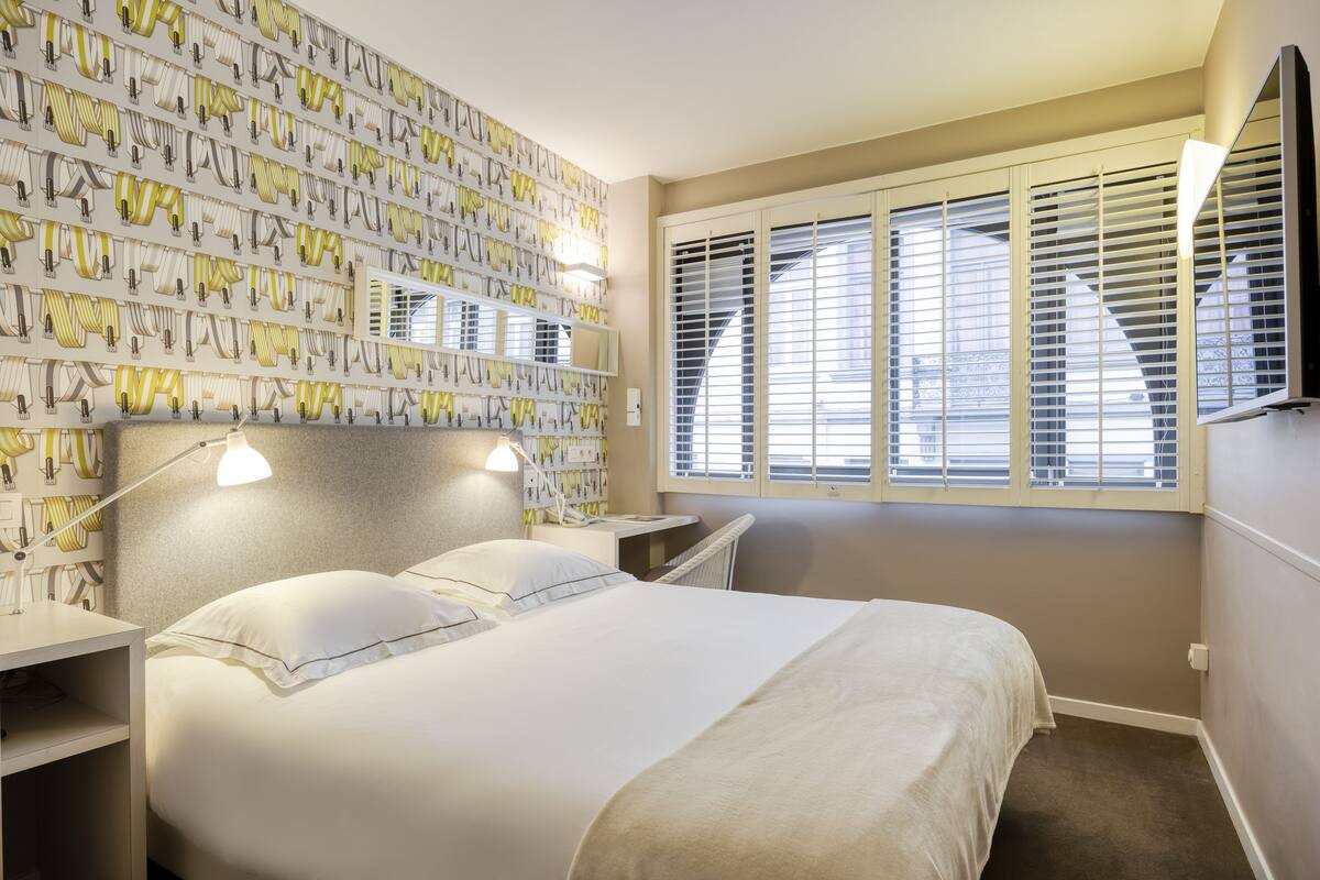 A neatly arranged bedroom with a large bed, bedside tables, and a wall-mounted TV.
