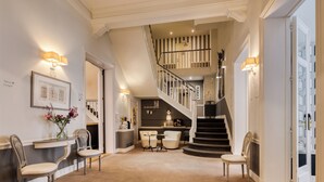 Un hall d’entrée spacieux avec un grand escalier, un comptoir d’accueil et un espace salon.