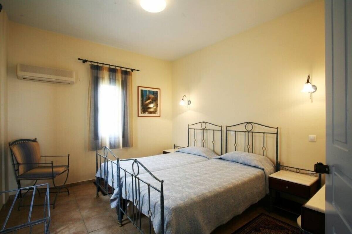 A bedroom with a single bed, a chair, a nightstand, and a wall-mounted air conditioner.