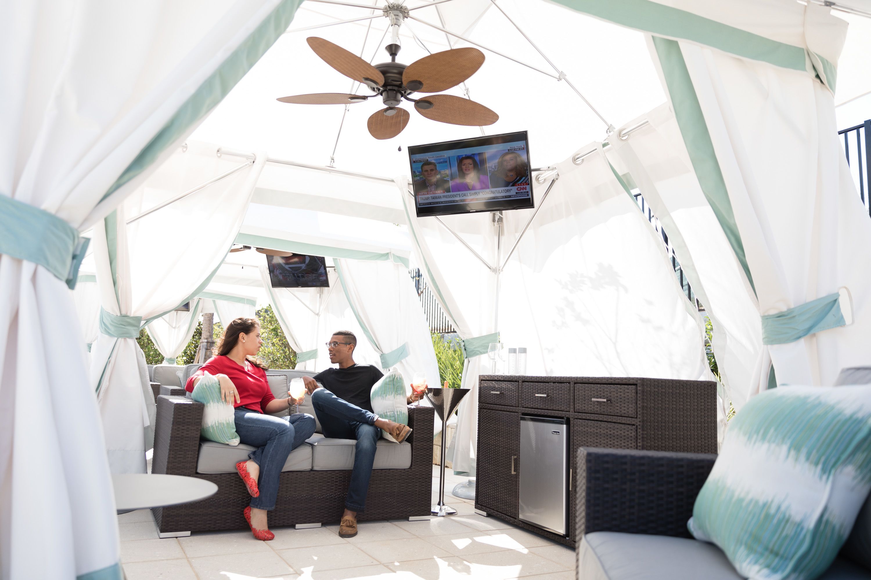 Een overdekte buitenruimte met een ventilator, een televisie en een kitchenette.