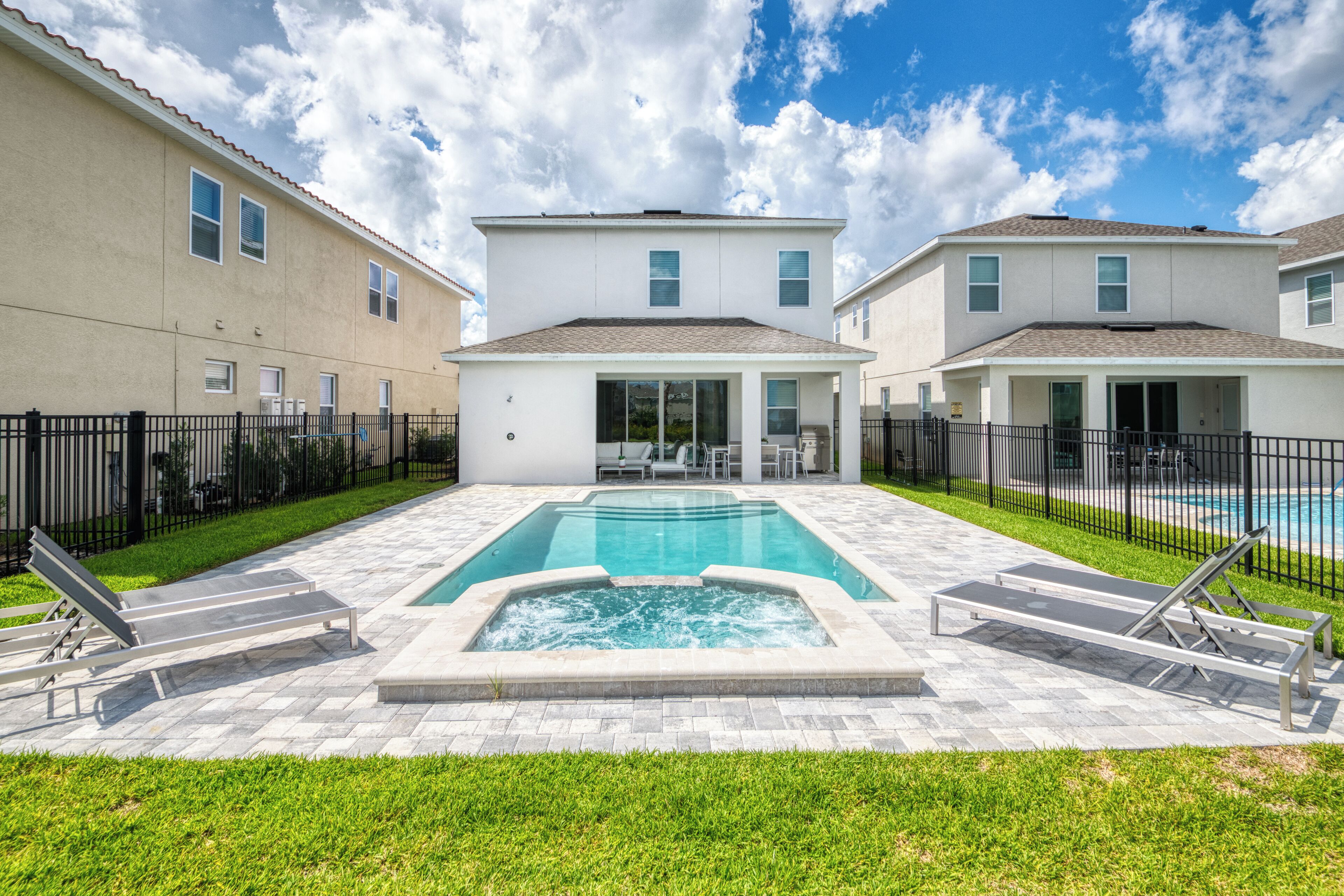 A residential area with a swimming pool, lounge chairs, and a paved patio.