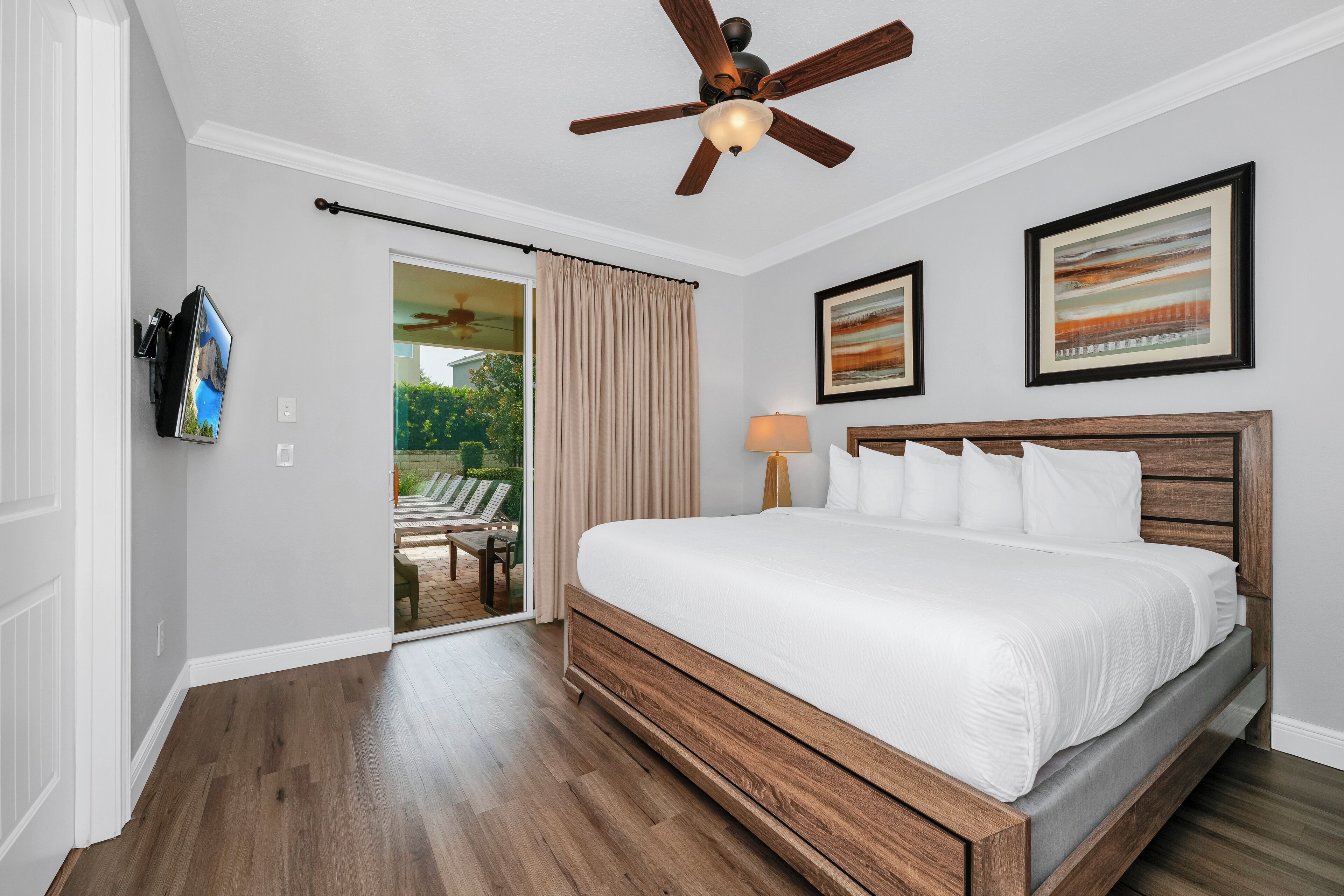Quarto com cama de madeira, ventilador de teto e porta de vidro deslizante para área externa.
