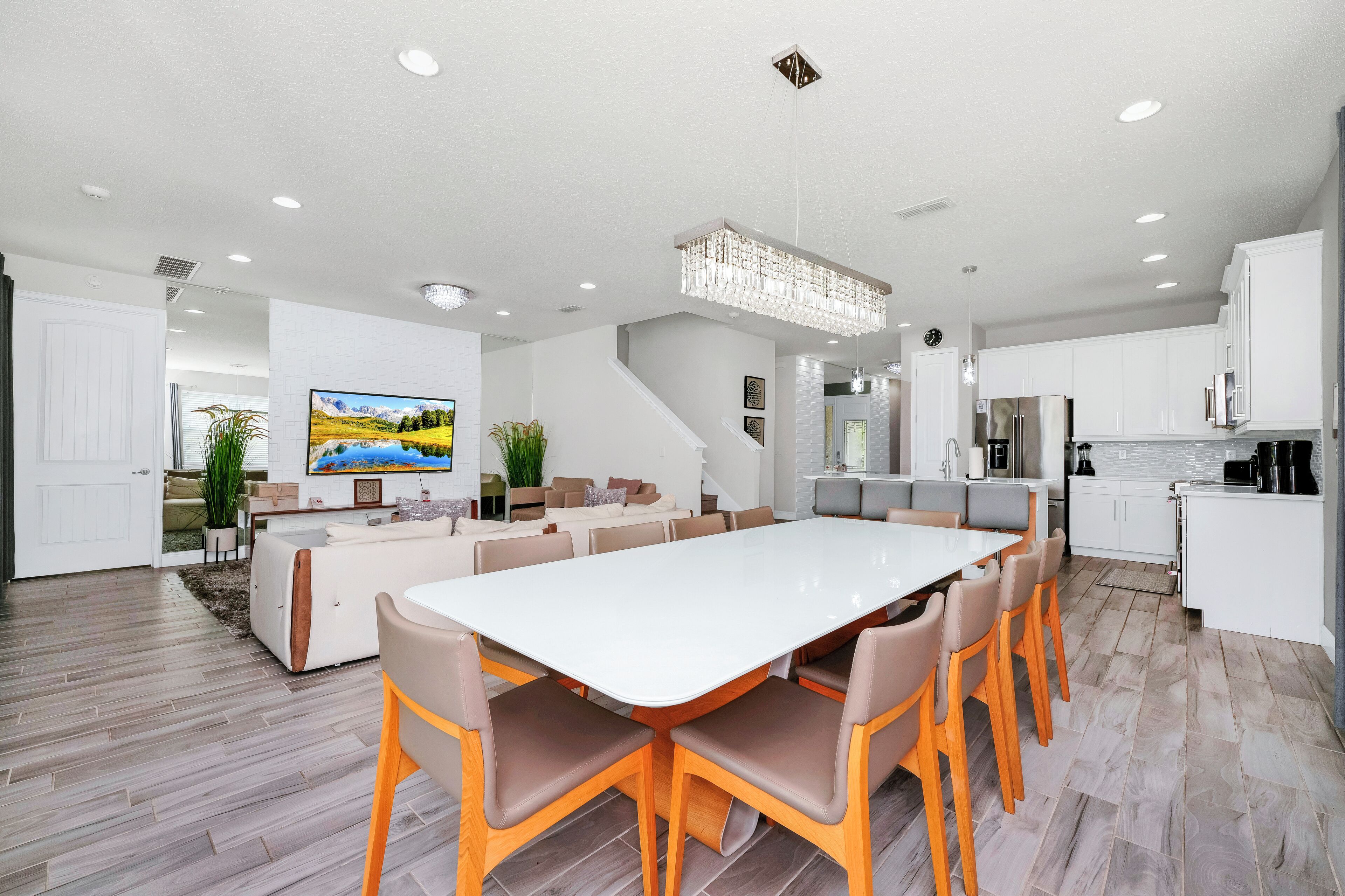 A modern kitchen with white cabinets, a large island, and a dining area with a white table and wooden chairs.