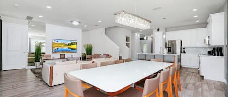A modern kitchen with white cabinets, a large island, and a dining area with a white table and wooden chairs.