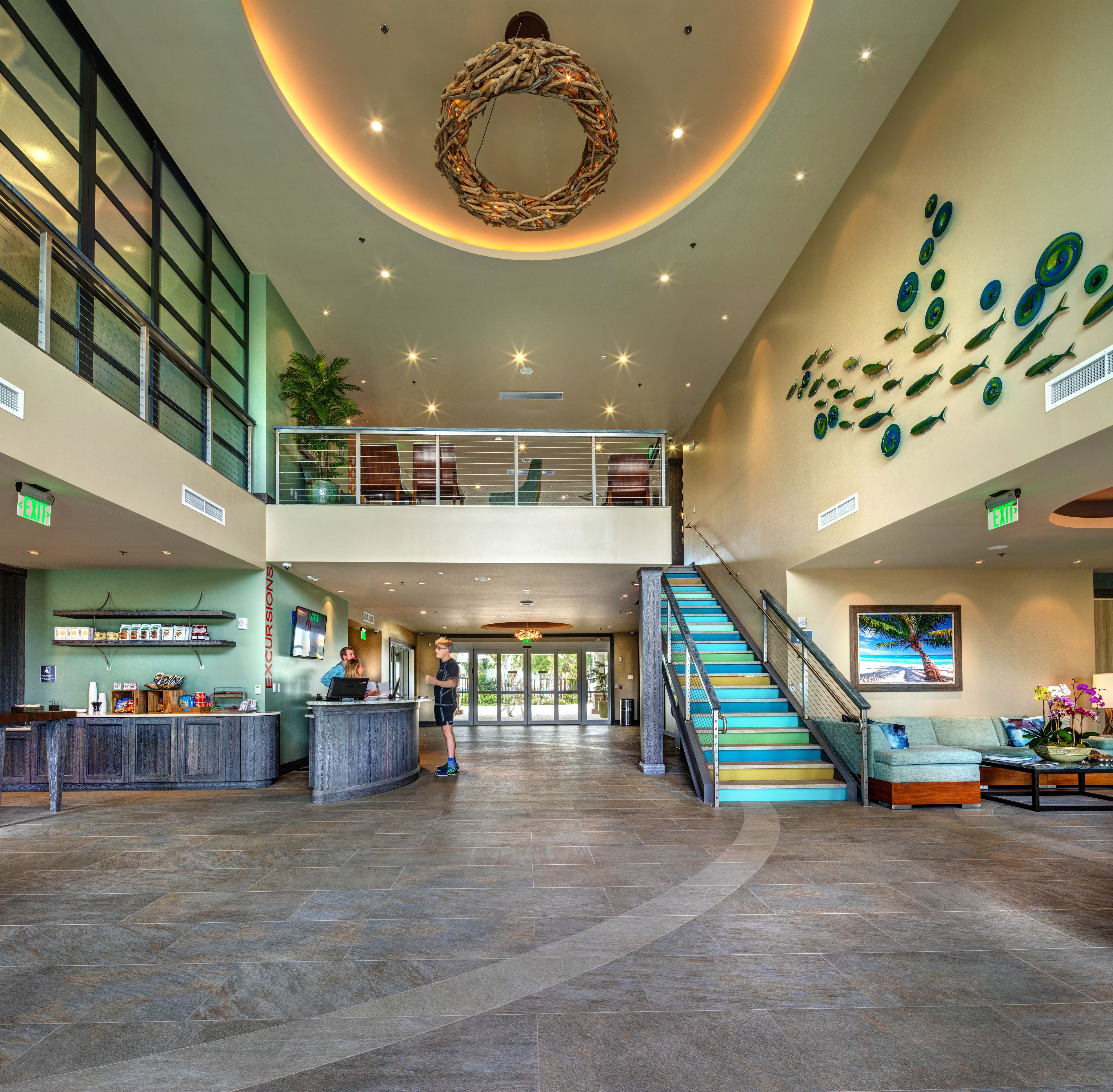 A spacious lobby with a central staircase, a reception desk, and a wall with fish decorations.