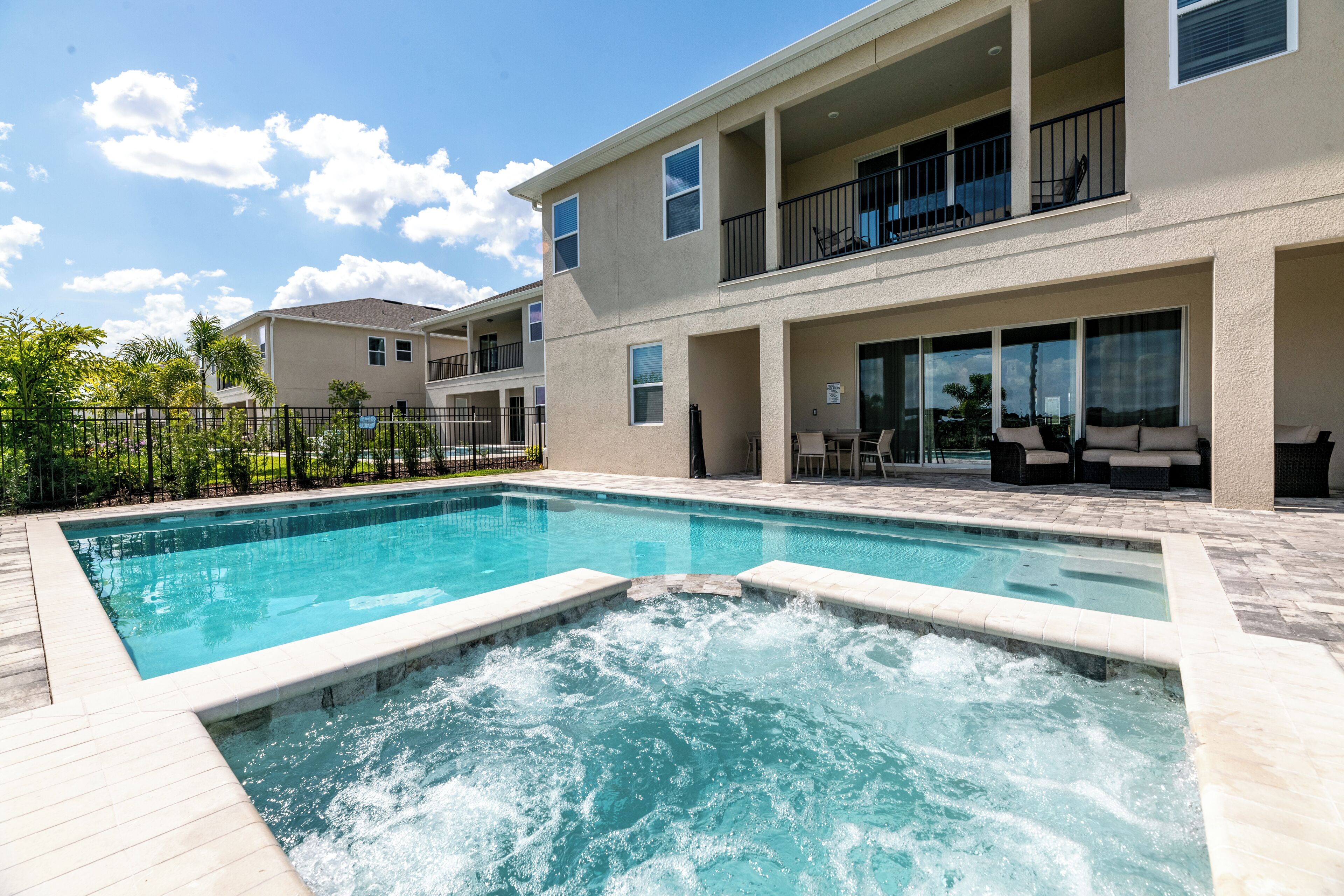 A swimming pool with a hot tub in the center, surrounded by a two-story building with balconies and outdoor seating.