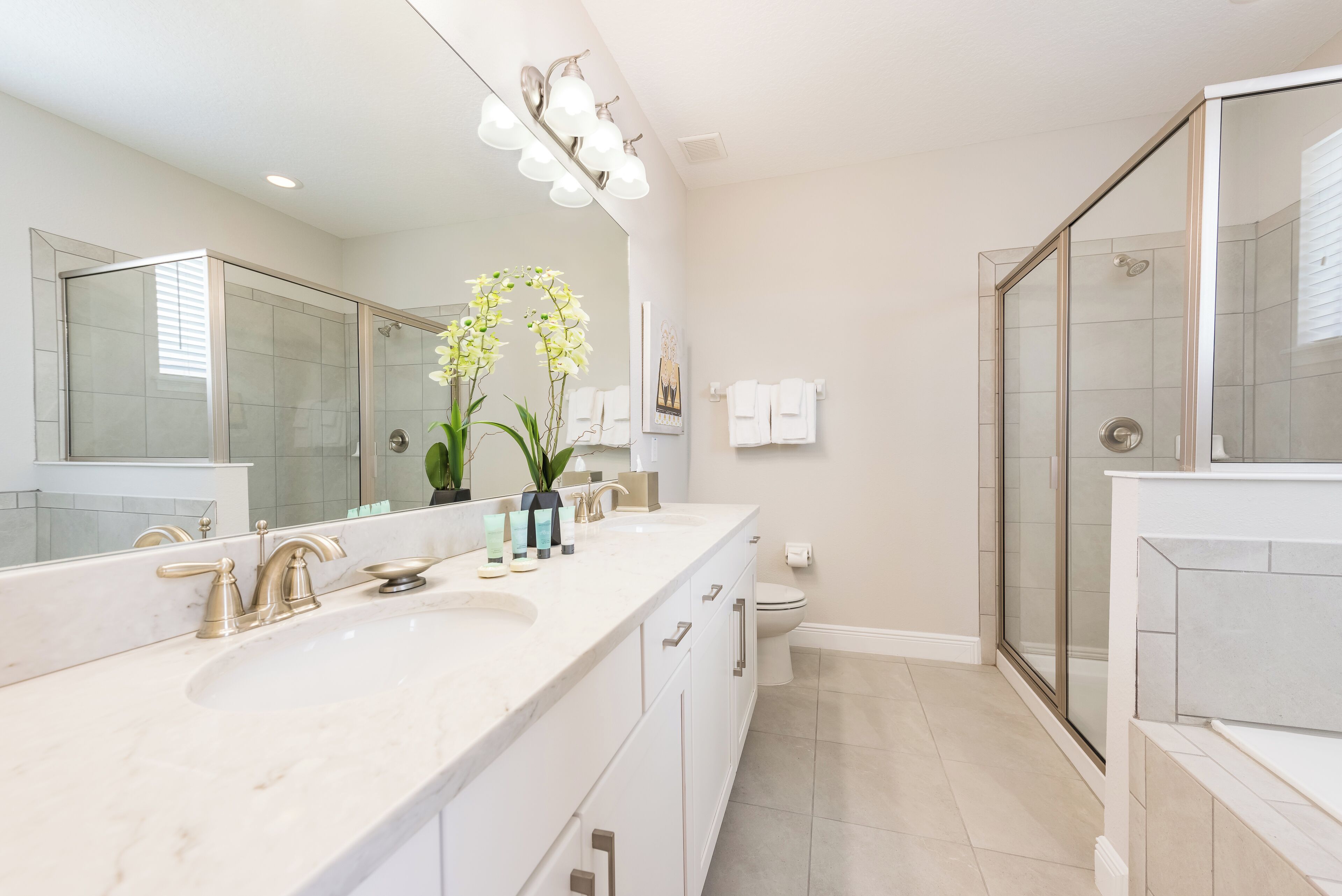 Une salle de bain moderne avec un grand miroir, un meuble-lavabo à deux vasques, une douche en verre et une plante orchidée en pot.