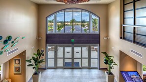 A spacious lobby with a high ceiling, a unique wooden chandelier, a large arched glass door leading outside, and potted plants. - Encore Resort and Water Park at Reunion by Rentyl (Kissimmee)