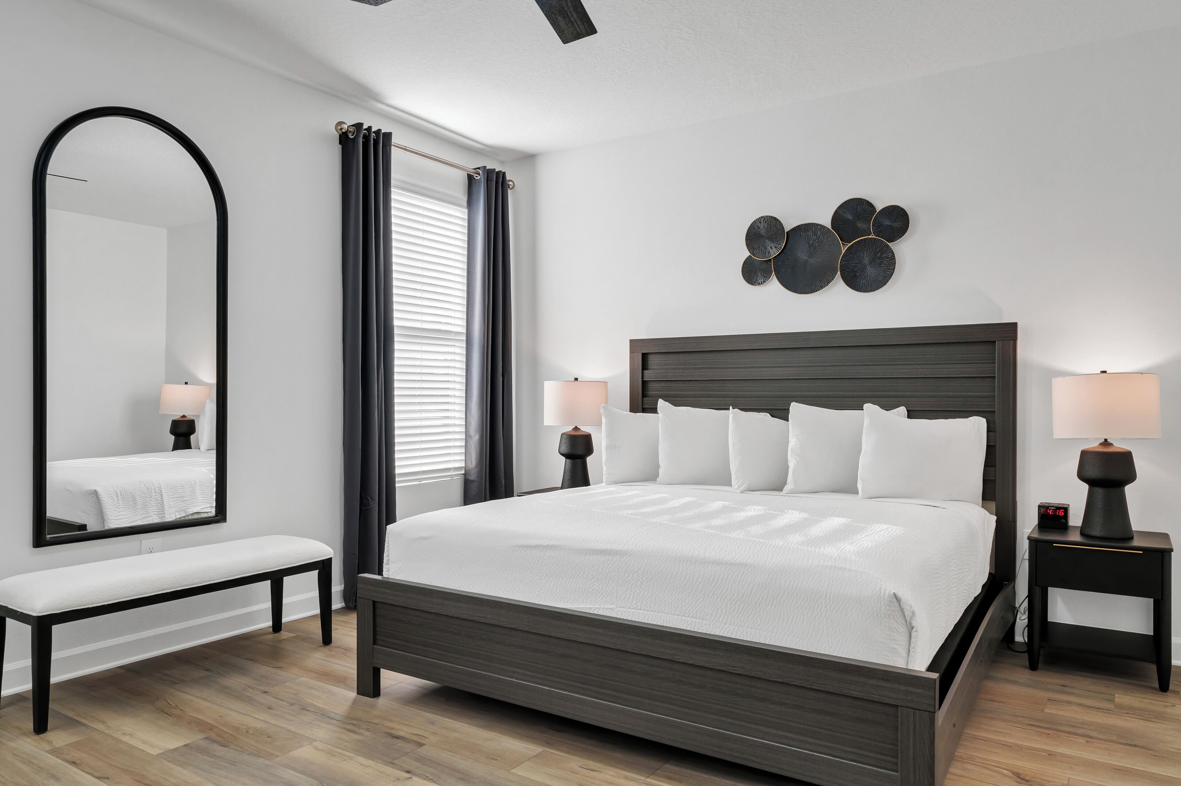 Ein modernes Schlafzimmer mit einem großen Bett, einer Bank, einem Spiegel und zwei Nachttischen mit Lampen.