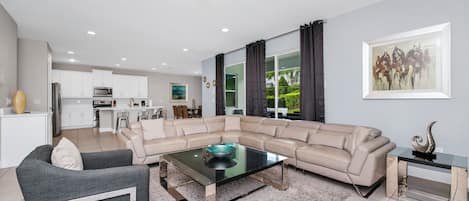 A modern living room with a sectional sofa, a glass coffee table, and a dining area in the background.