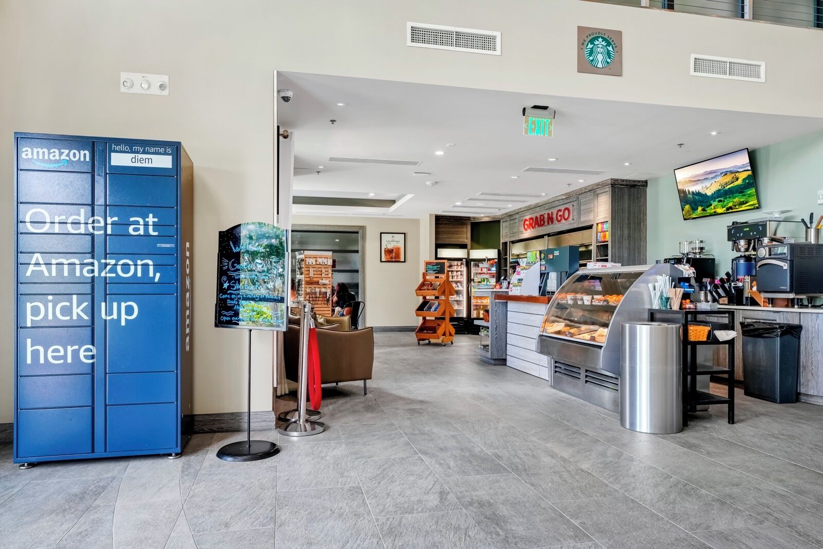 A modern interior with a 'Grab n Go' counter, a 'Hello, my name is diem' sign, and an Amazon locker.