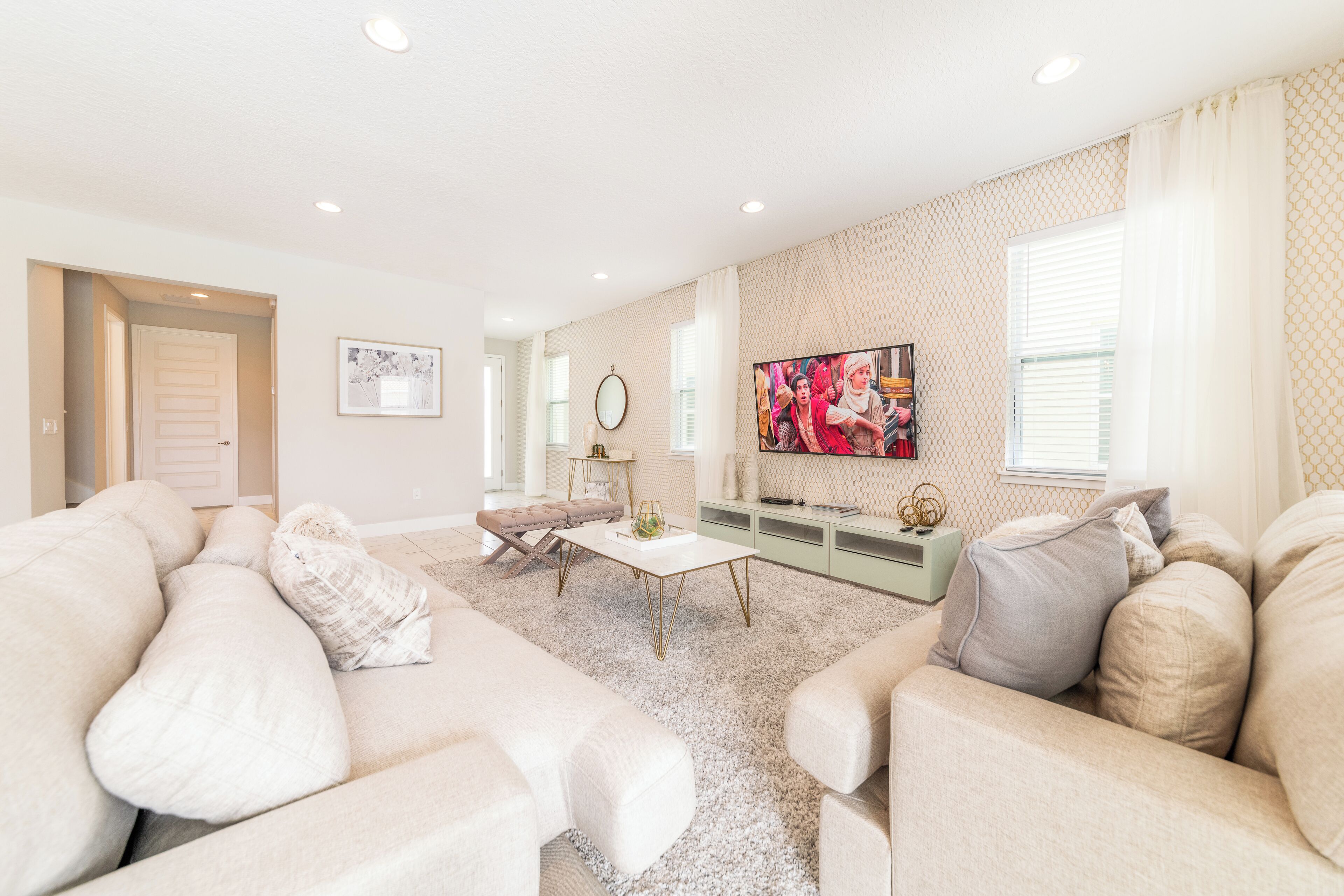 A spacious living room with a large sofa set, a coffee table, and a TV mounted on the wall.