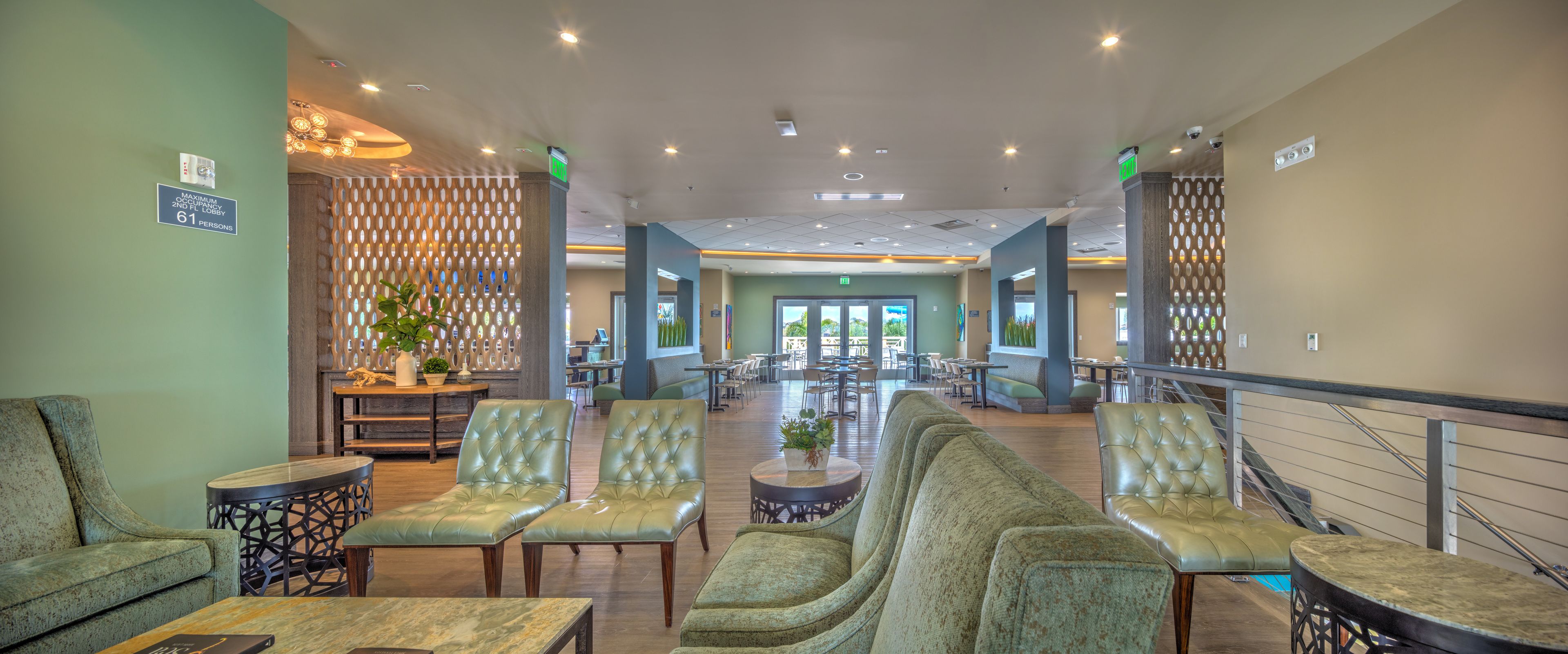 A spacious lobby with green upholstered chairs, a coffee table, and a decorative plant.