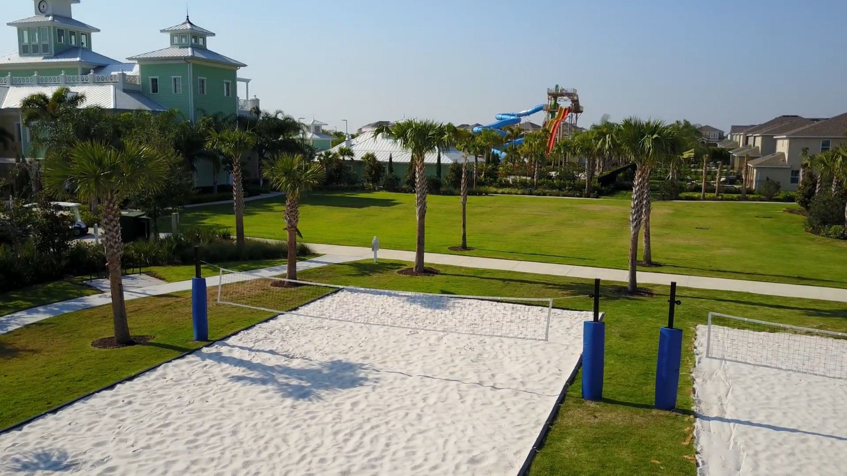 Una zona de playa arenosa con palmeras y un tobogán de fondo.