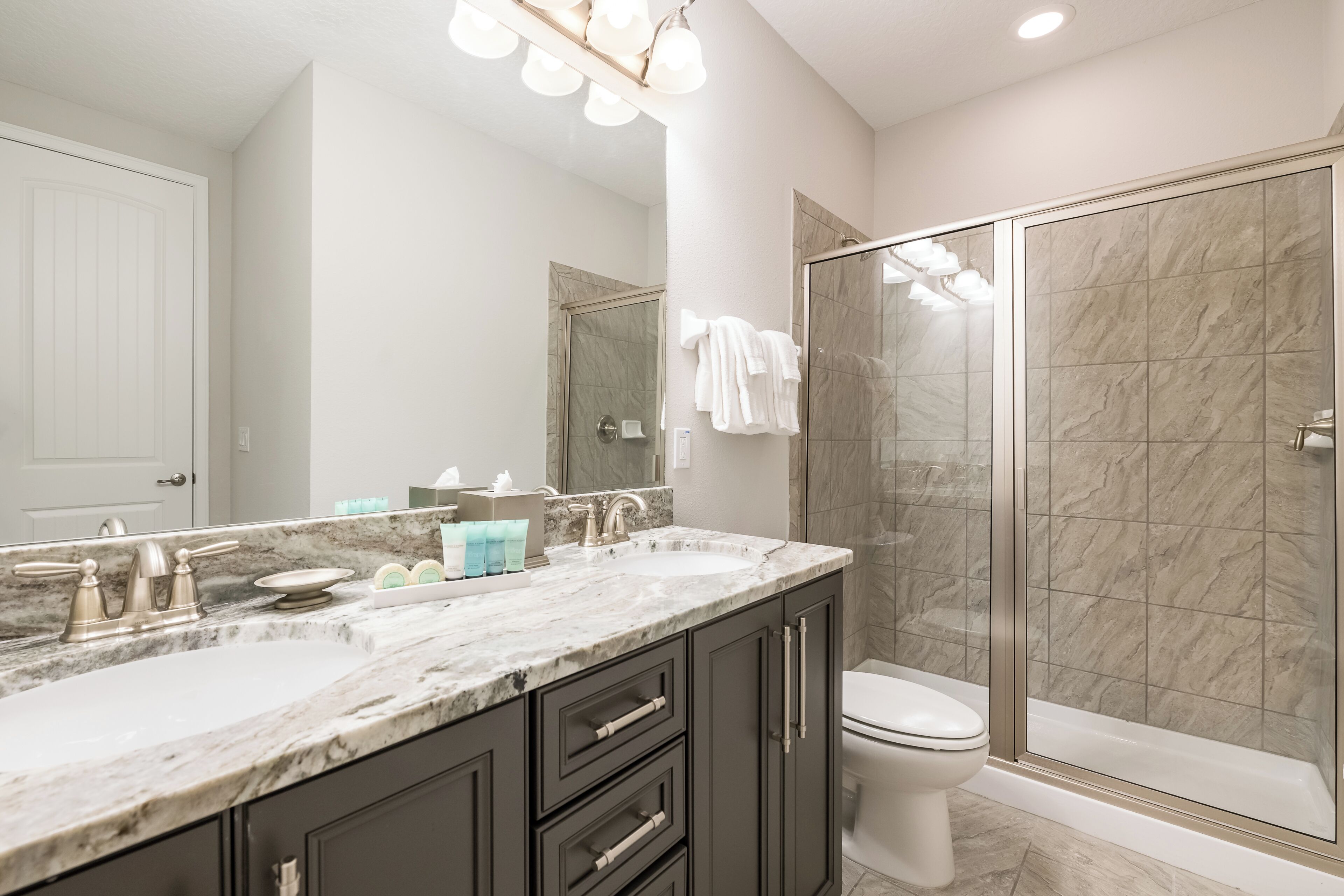 A modern bathroom with a double sink vanity, a toilet, and a glass-enclosed shower.