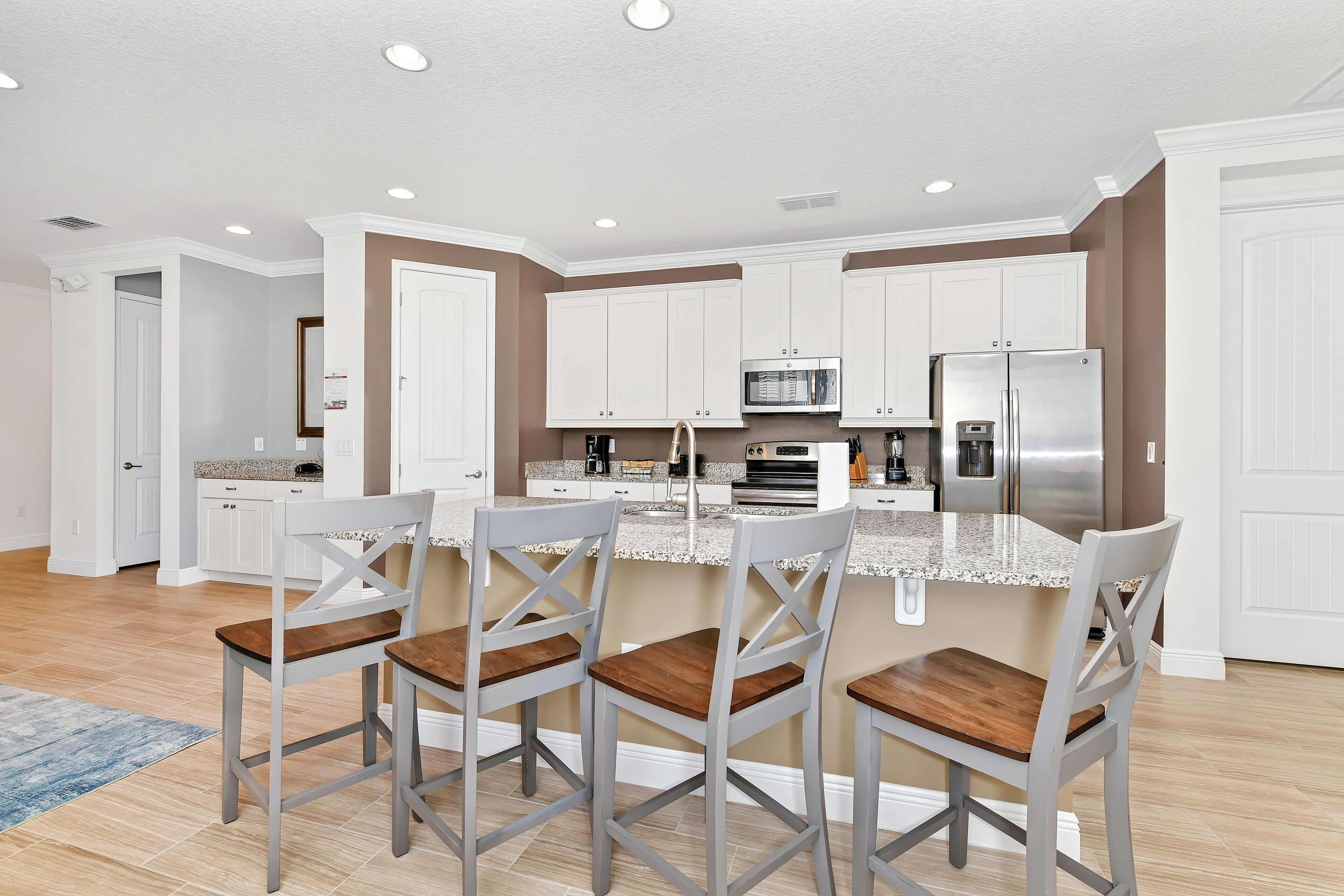 A modern kitchen with white cabinets, a granite countertop, and stainless steel appliances. There are three bar stools with wooden seats.
