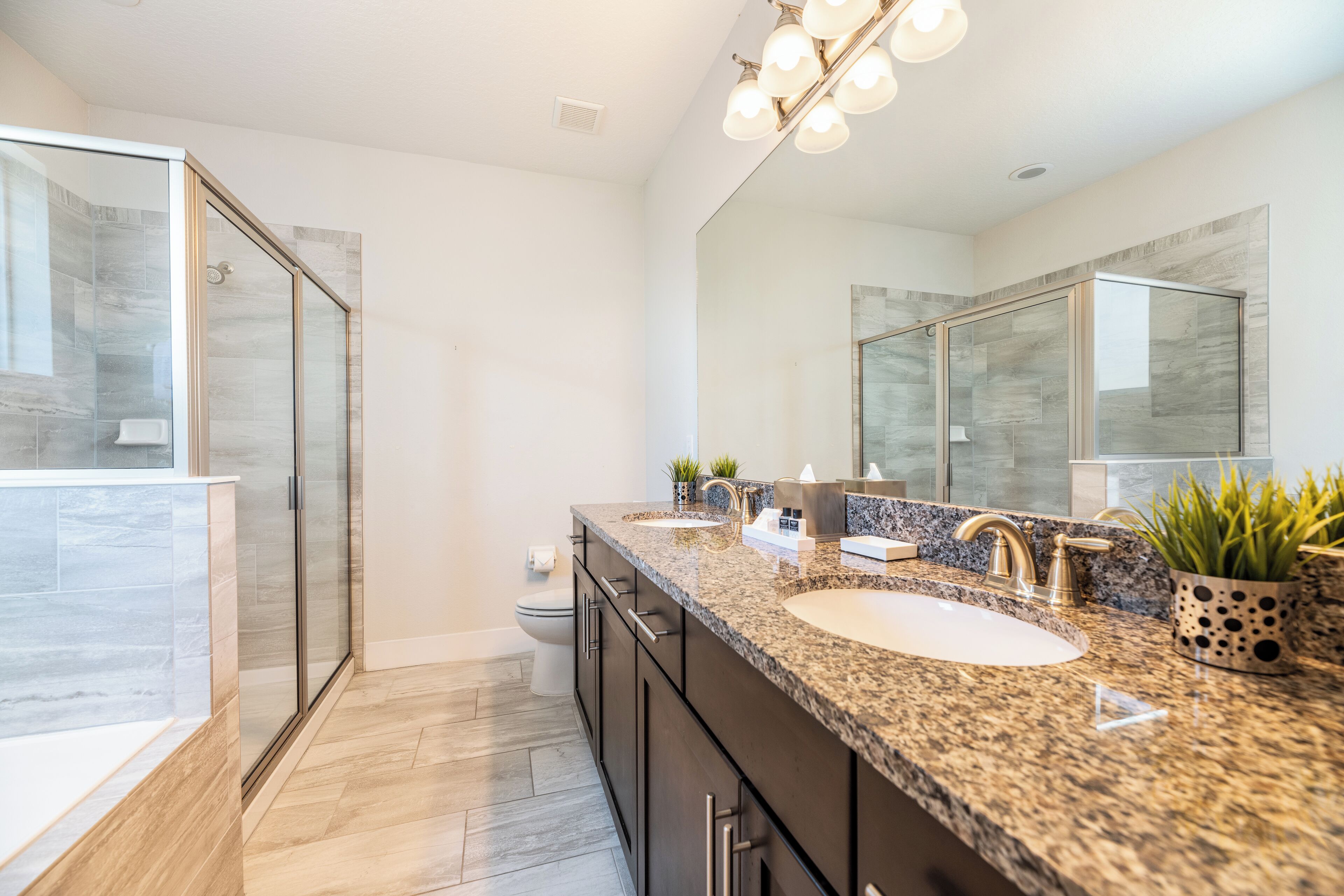 A modern bathroom with a glass shower enclosure, a large vanity with a granite countertop, and a large mirror.