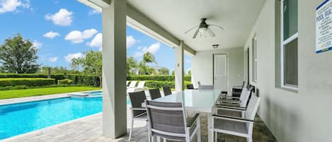 A covered outdoor area with a pool, a table with chairs, and a ceiling fan.