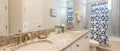 A bathroom with two sinks, a mirror, a shower with a geometric-patterned curtain, and a toilet.
