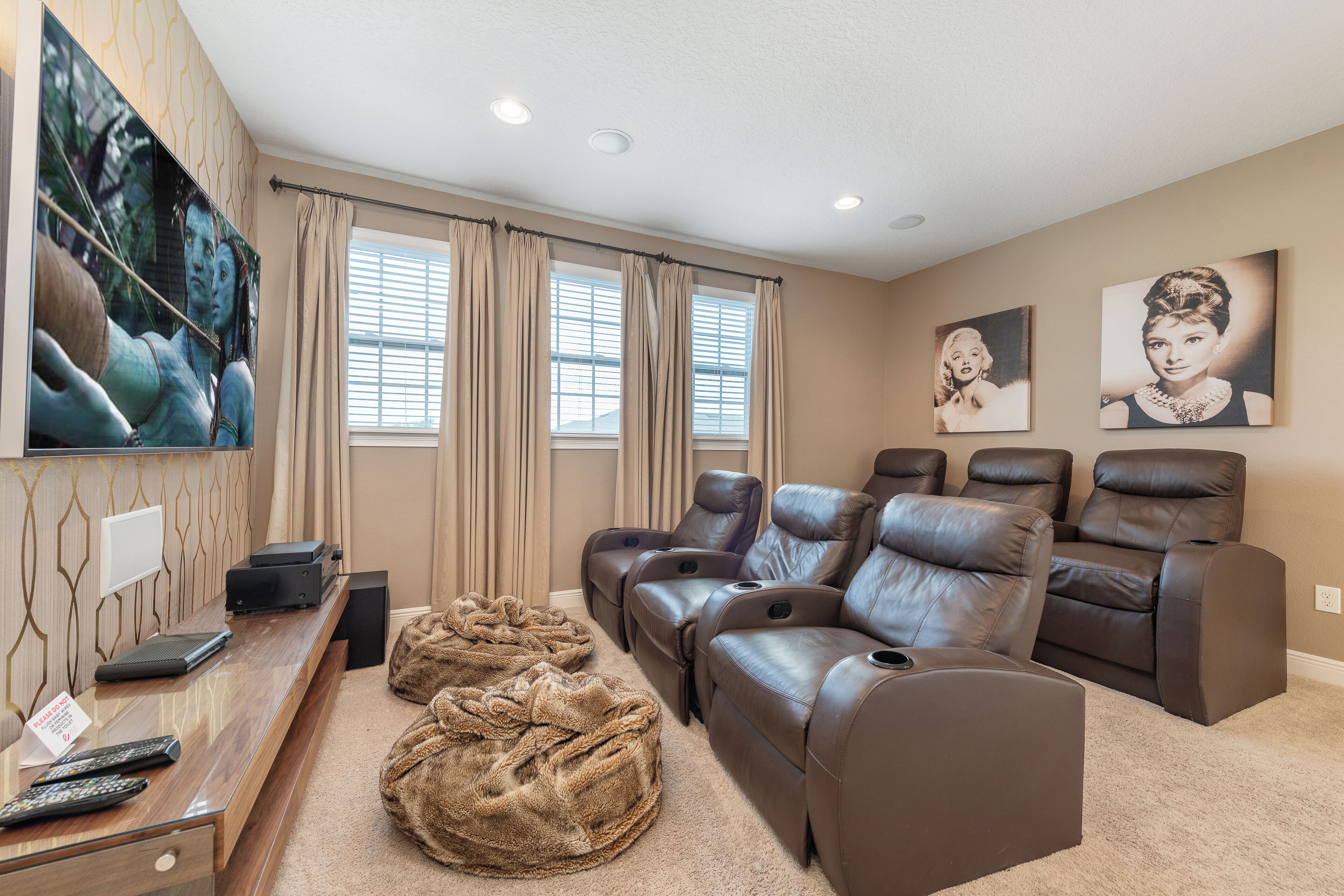 A home theater room with a large flat-screen TV, multiple leather recliners, a plush bean bag, and a carpeted floor.