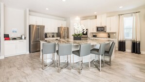 A modern kitchen with white cabinets, stainless steel appliances, and a marble island with four bar stools. - Encore Resort and Water Park at Reunion by Rentyl (Kissimmee)