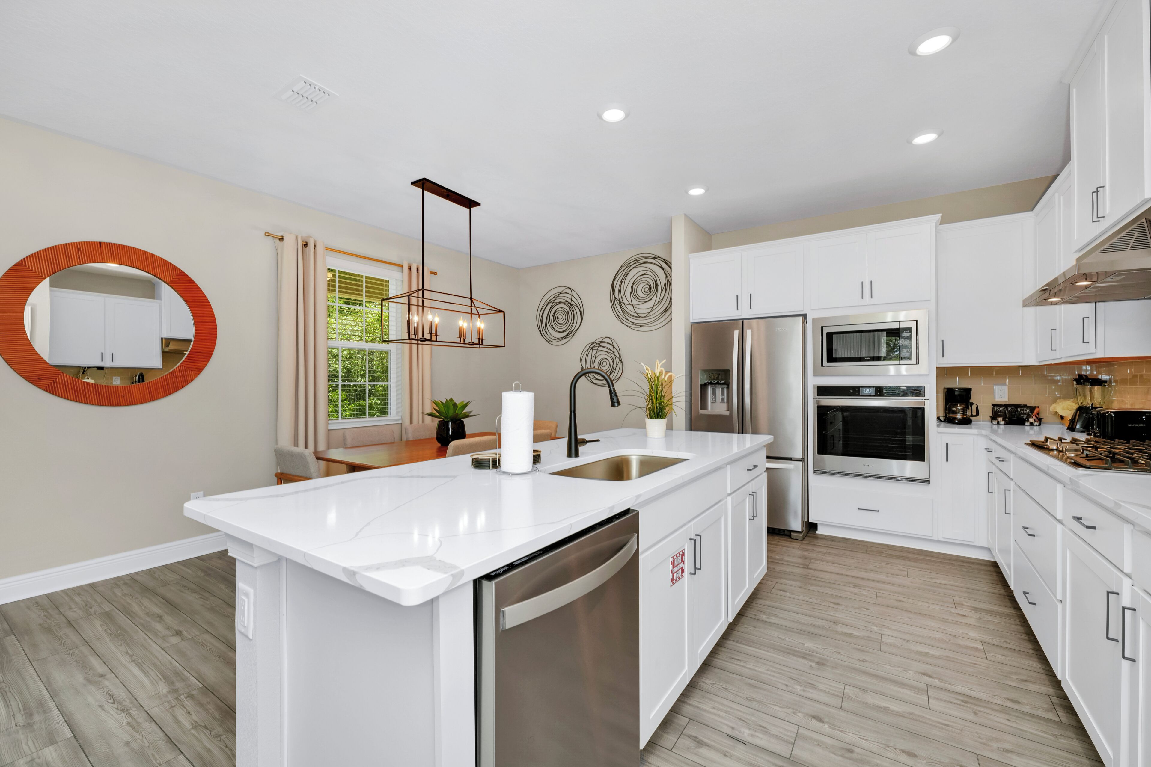 A modern kitchen with white cabinetry, a central island, stainless steel appliances, and decorative wall art.